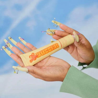 Best antioxidants for skin featured in a Topicals Like Butter cream held by hands with bold nail art against a sky background